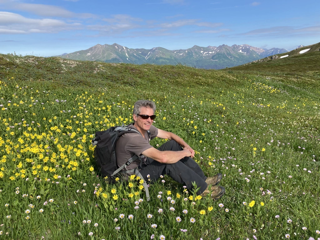 Thomas Pease sitting on a vibrant meadow in Alaska mountains